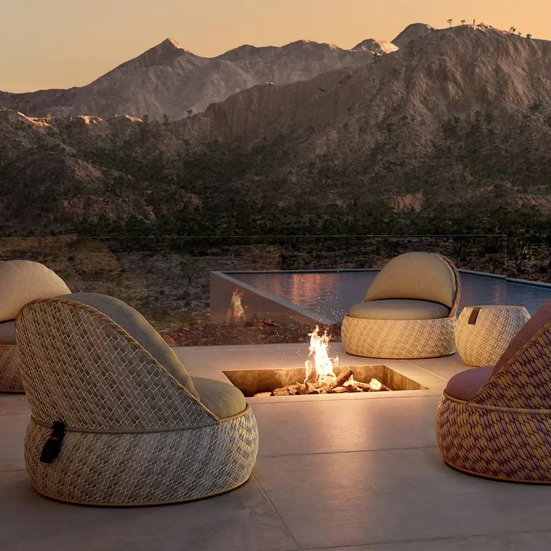 Dedon Dala woven lounge chairs gathered around a fire pit on a terrace at dusk, mountains beyond