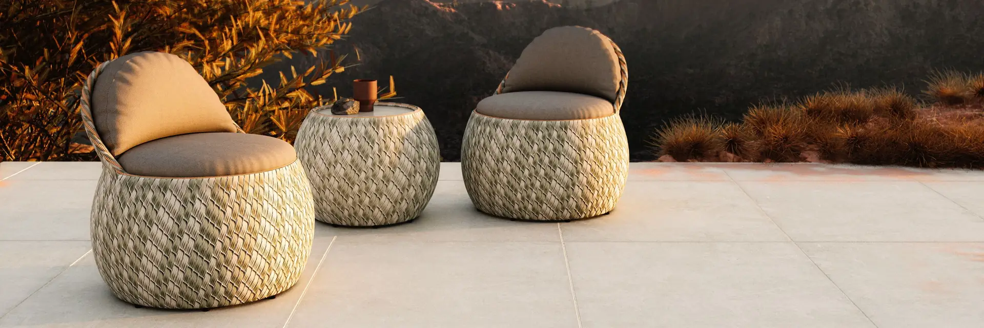 Dedon Dala woven lounge chair and stools on a stone terrace overlooking mountains at sunset