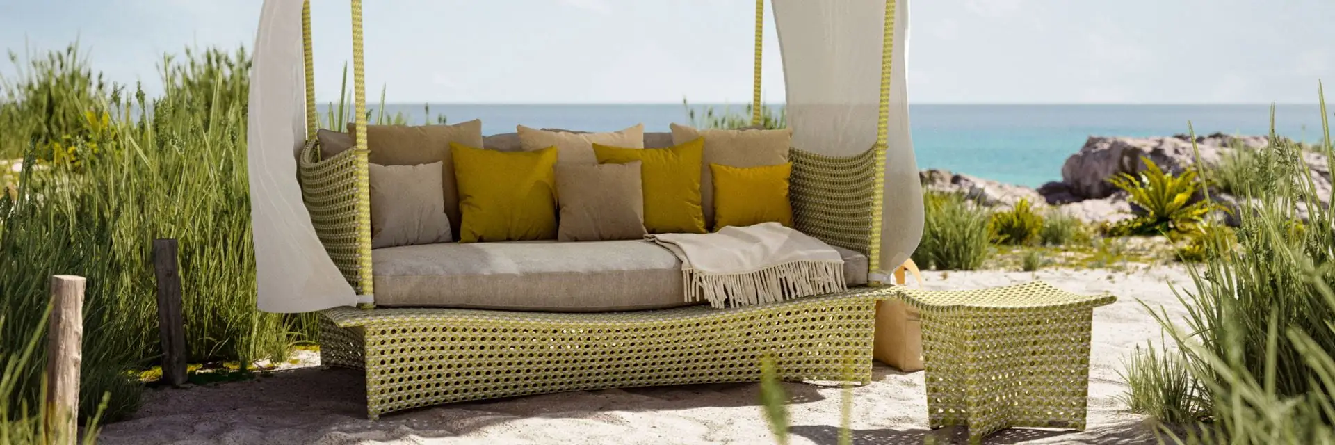Dedon Daydream four-poster daybed with a white canopy and yellow cushions among dune grass on a beach
