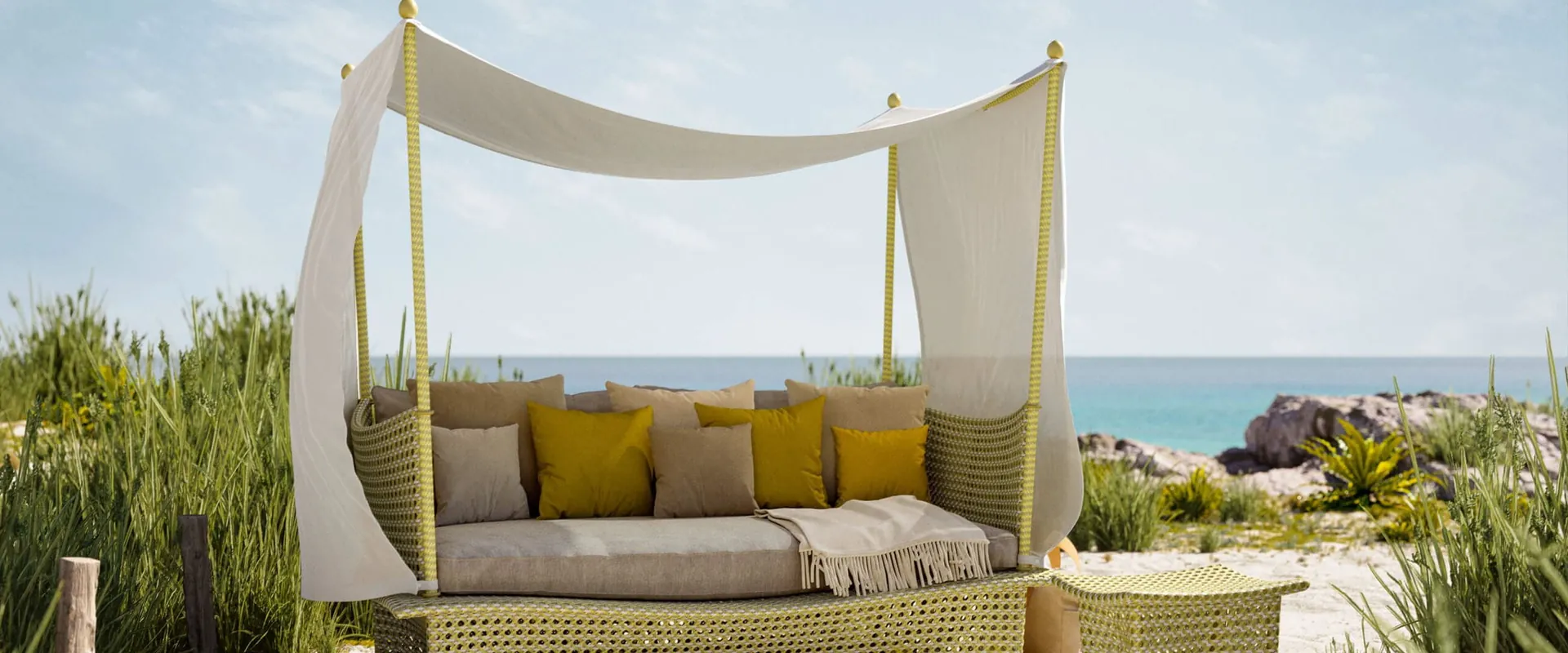 Dedon Daydream four-poster daybed with a white canopy and yellow cushions among dune grass, the sea behind