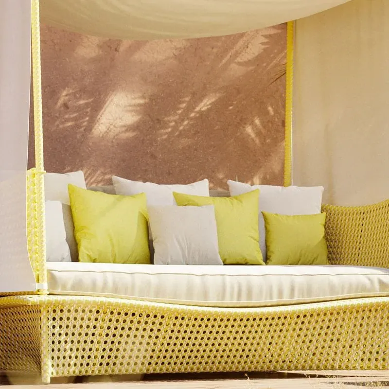Close view of a Dedon Daydream daybed in woven fiber with white and yellow cushions under its canopy