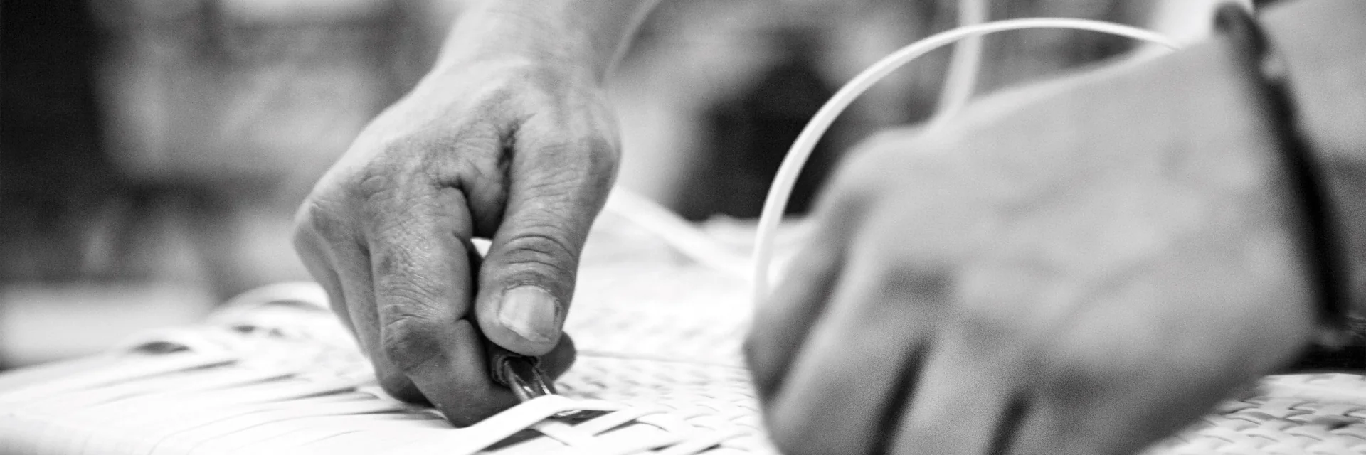 Black-and-white close-up of hands weaving Dedon fibre onto a furniture frame