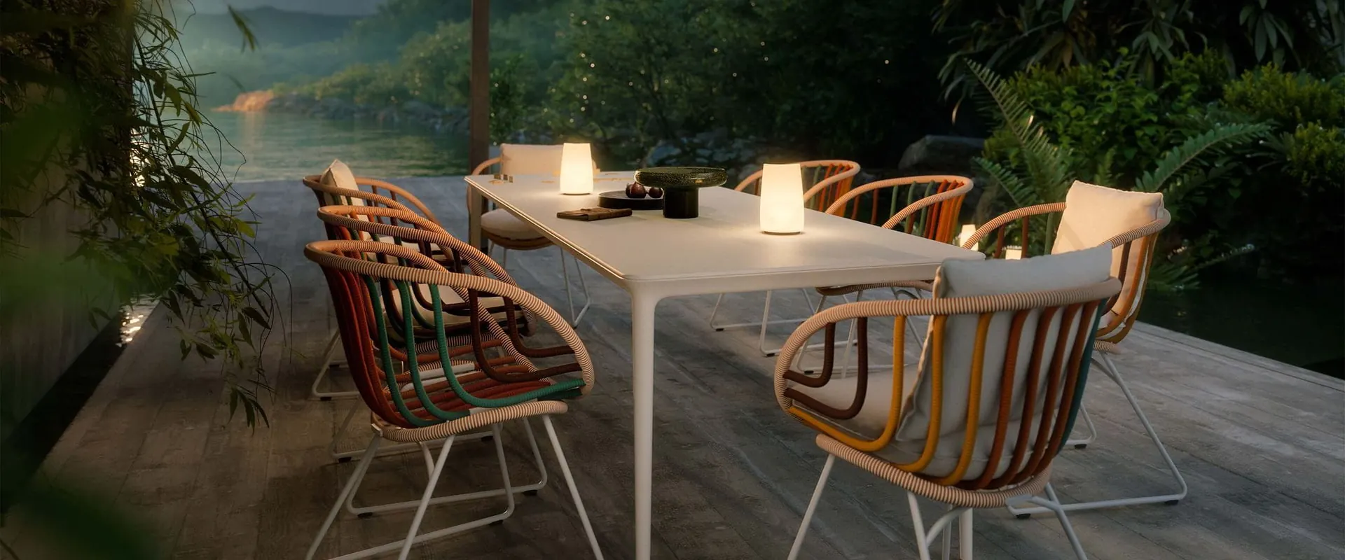 Dedon Kida dining armchairs with colorful woven frames along a white table with lamps at dusk, by a lake