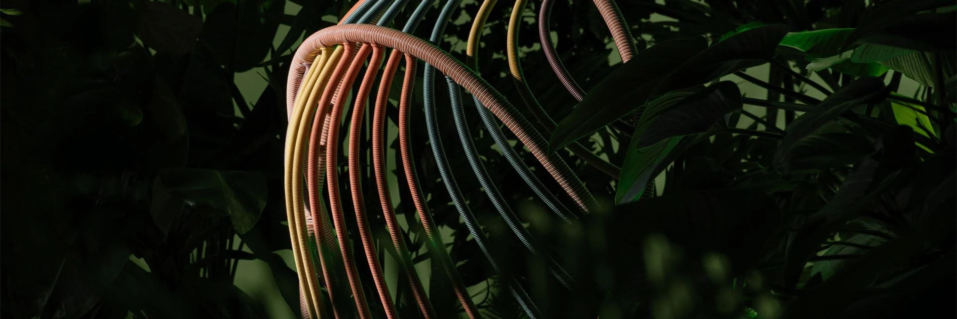Dedon Kida hanging lounge chair with coloured cords, seen against dark foliage