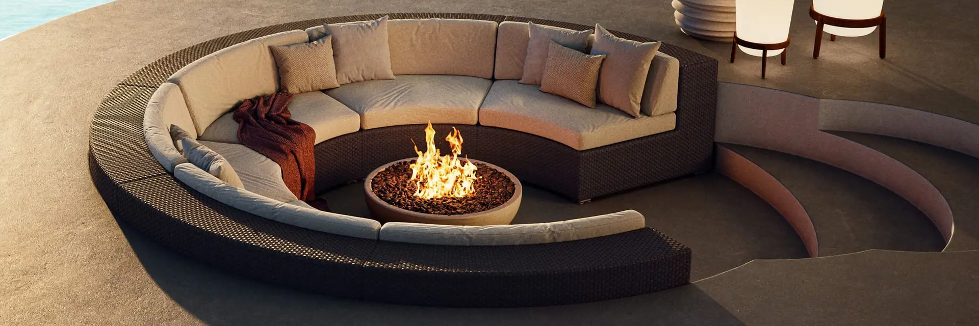 Dedon Loon round sofa sunk into the sand around a fire pit, beside a turquoise lagoon