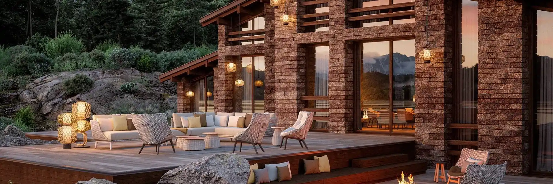 Dedon lounge furniture on the timber deck of a mountain lodge with lit windows at dusk