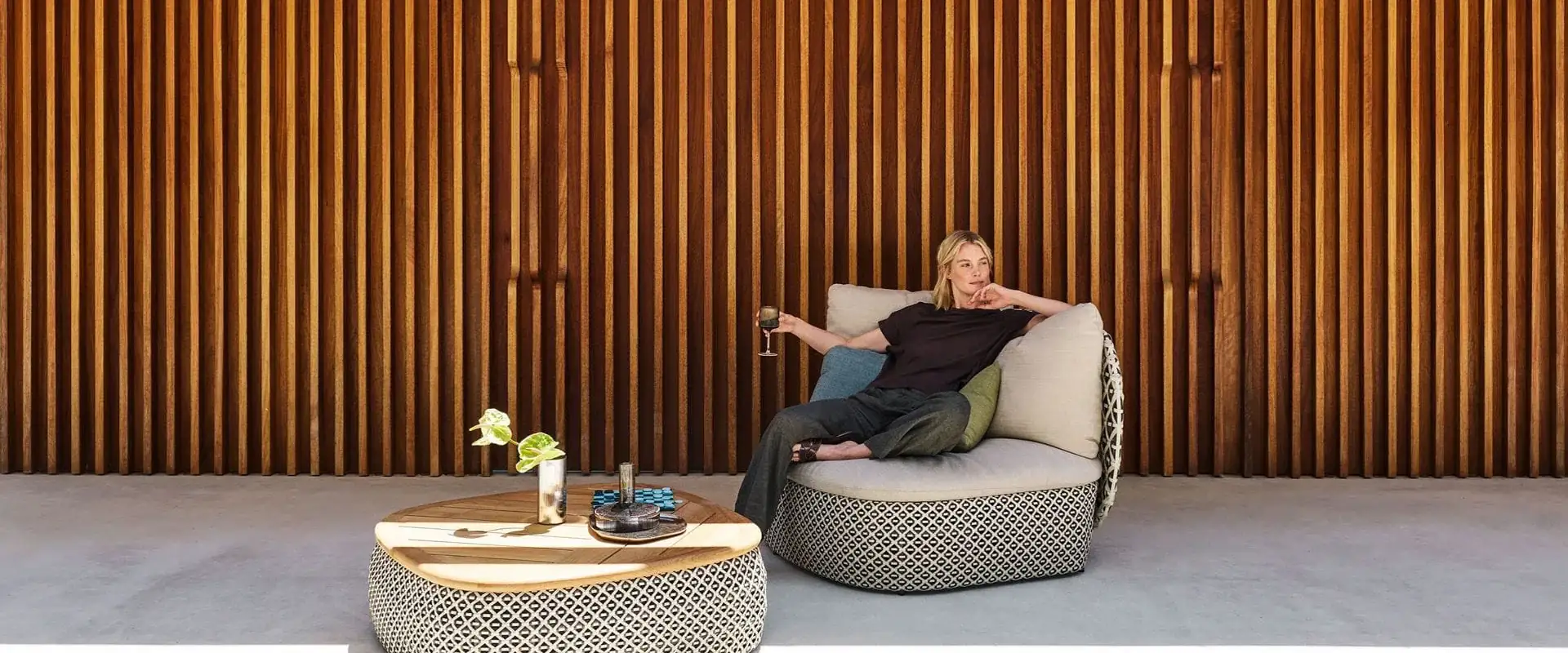 Dedon Mdear lounge chair and coffee table in a black-and-white weave before a wooden slat wall, a woman seated in the chair
