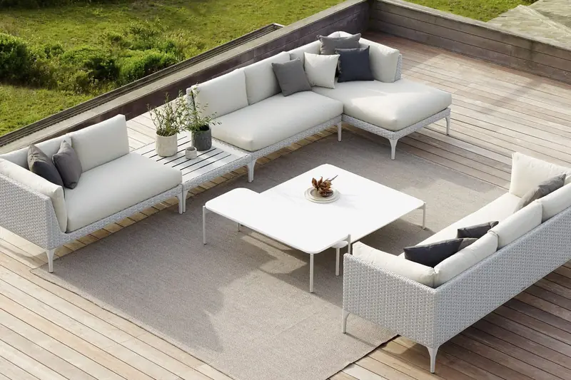 Dedon MU modular sofa in white with a low table on a timber deck beside a lawn, seen from above