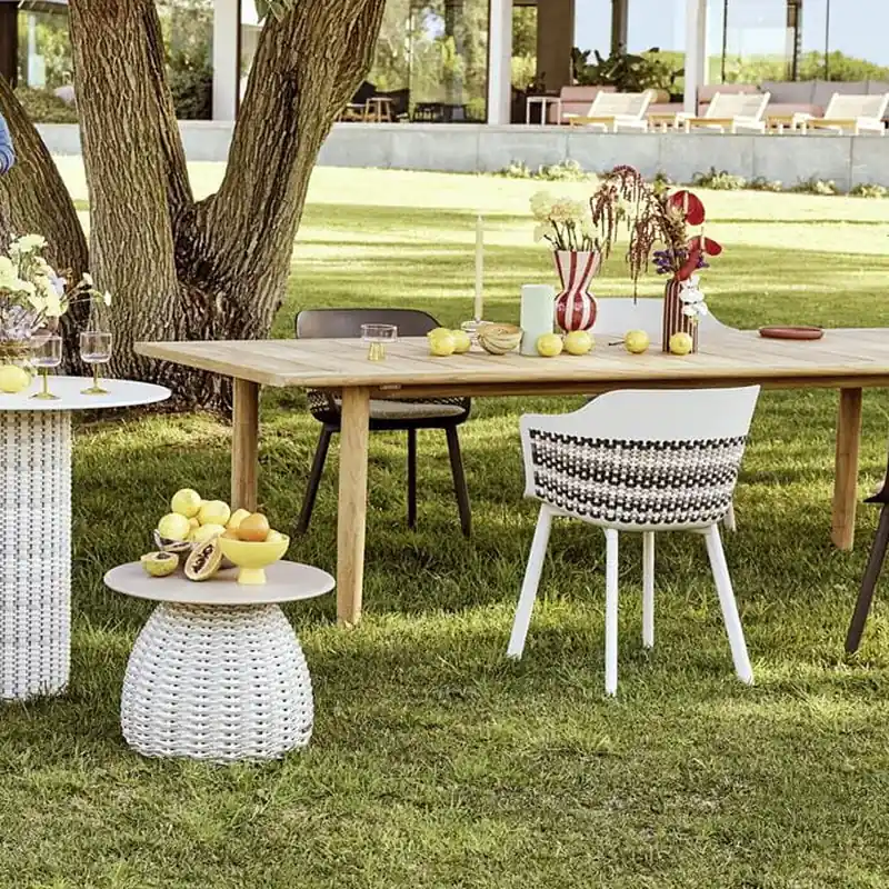 Dedon Mymi chairs with patterned weave around teak tables set for lunch under a large tree in a garden