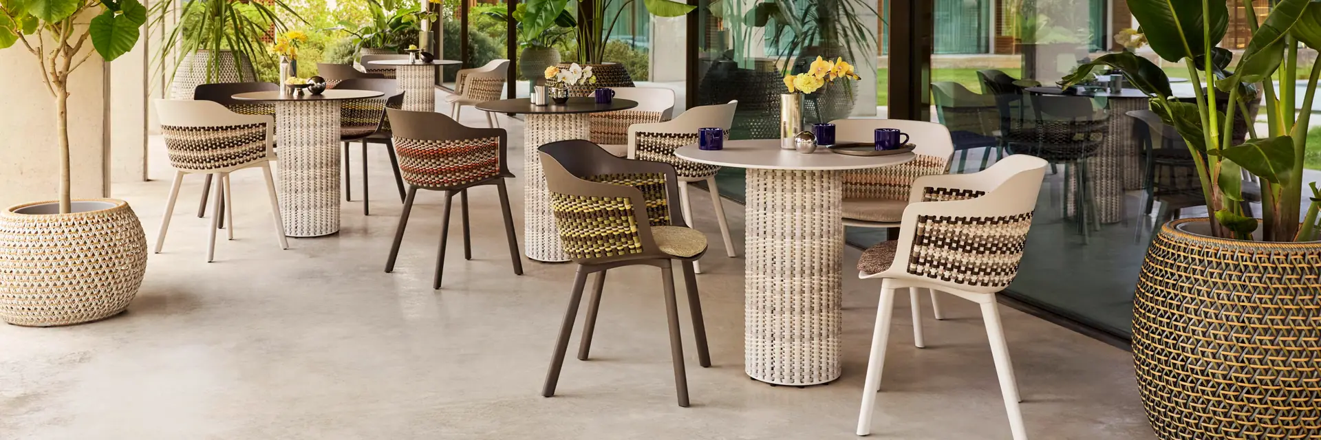 Dedon Mymi dining chairs around round tables with woven bases on a covered terrace with a timber ceiling and large planters