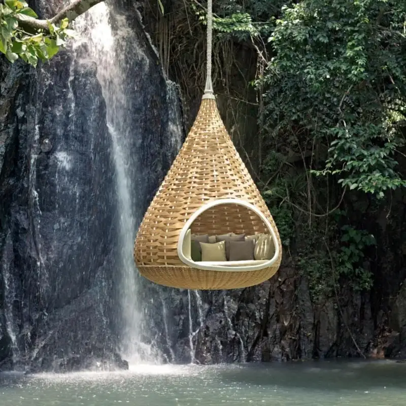 Dedon Nestrest hanging lounger in natural weave suspended over a pool beside a waterfall