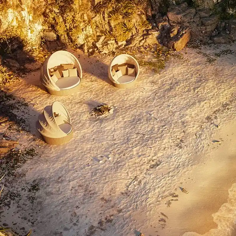 Three Dedon Orbit round loungers on the sand of a small cove, seen from above in evening light