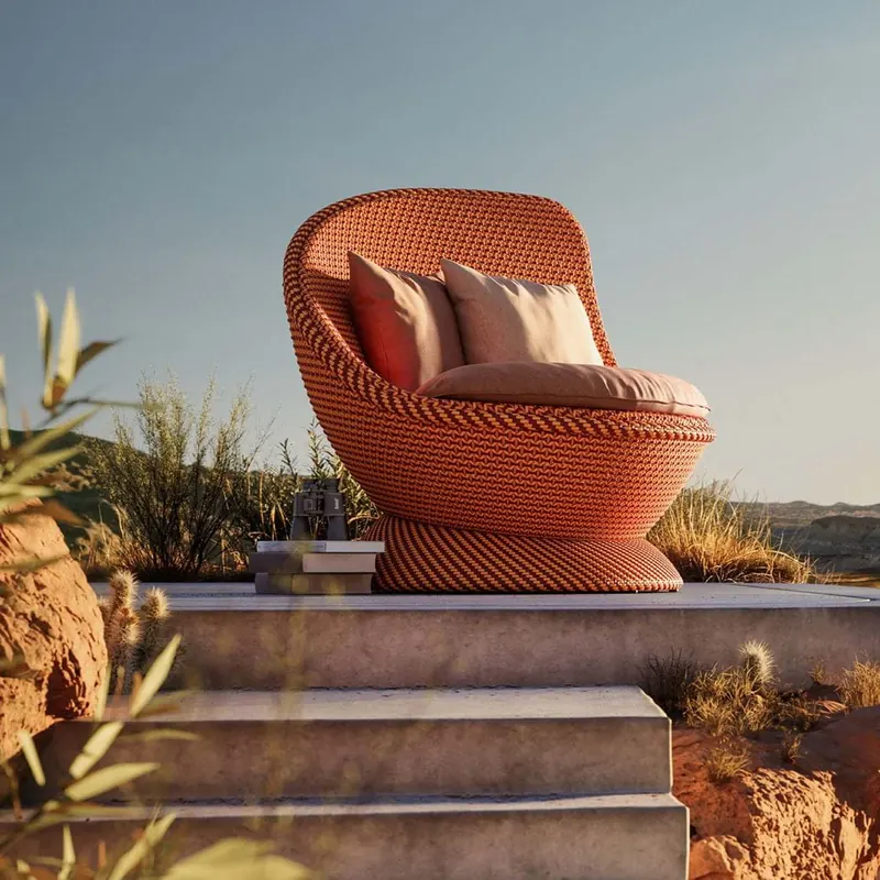 Dedon Papyon lounge chair in coral weave with cushions on a stone platform above a desert canyon