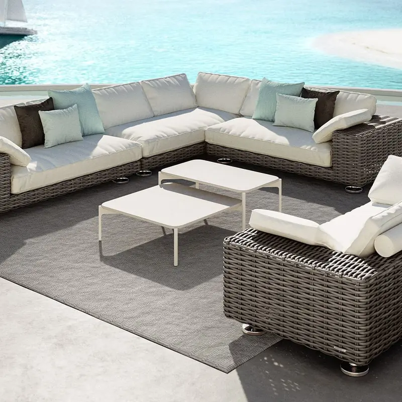 Two Dedon Paros corner sofas in gray weave with white cushions around low tables on a waterfront terrace