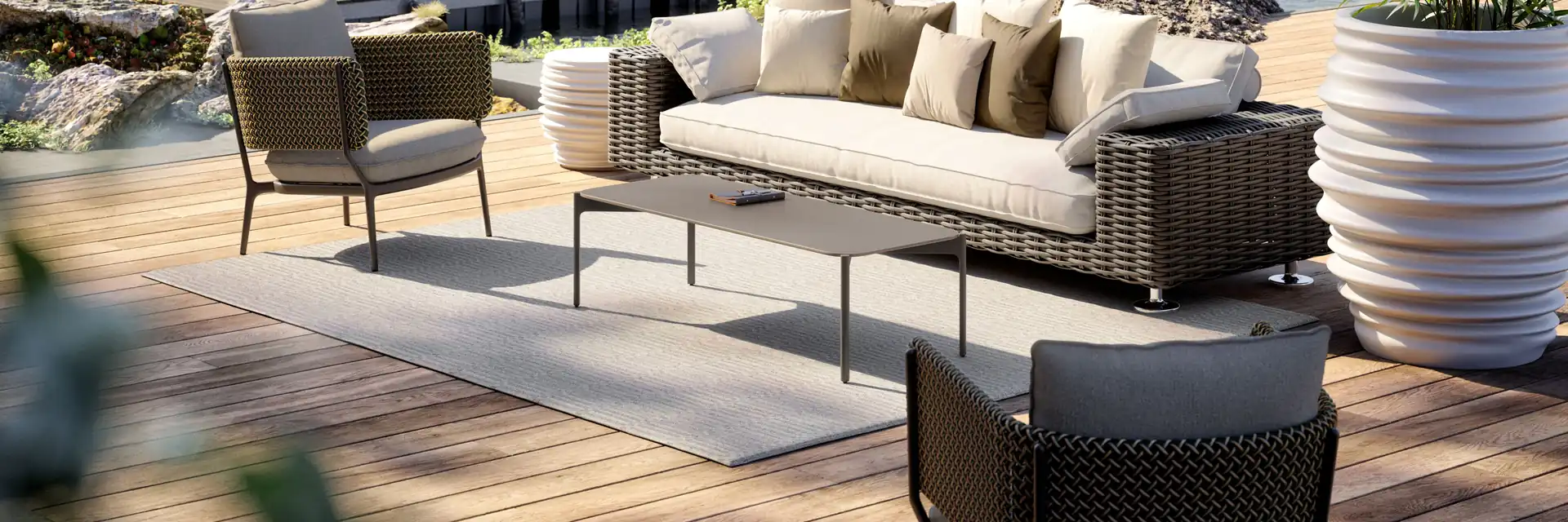 Dedon Paros woven sofa, armchair and coffee table on a timber deck beside a lake, with a jetty and wooded hills behind