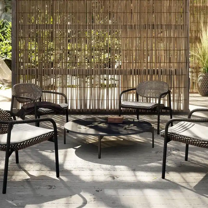Dedon Roii lounge chairs with dark frames around a low table on a sunlit deck, a bamboo screen behind