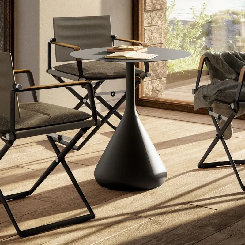 Dedon Satellite round table on a cone-shaped base with two folding director's chairs on a sunlit wooden floor