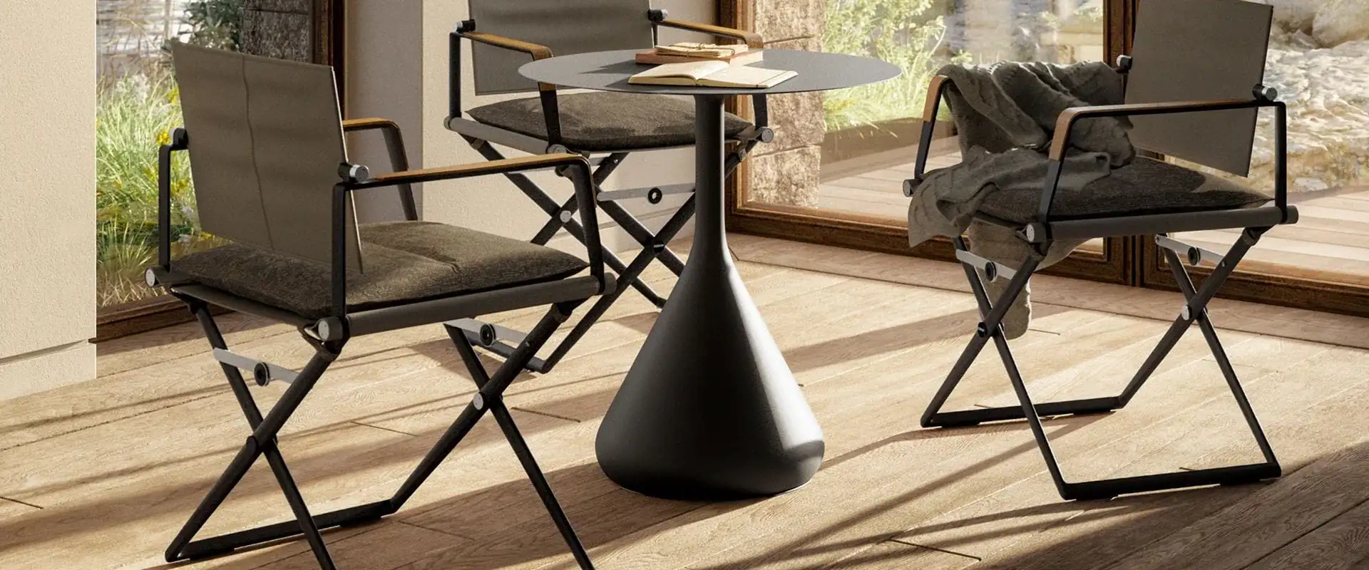 Dedon Satellite round table on a cone-shaped base with two folding director's chairs on a sunlit wooden floor