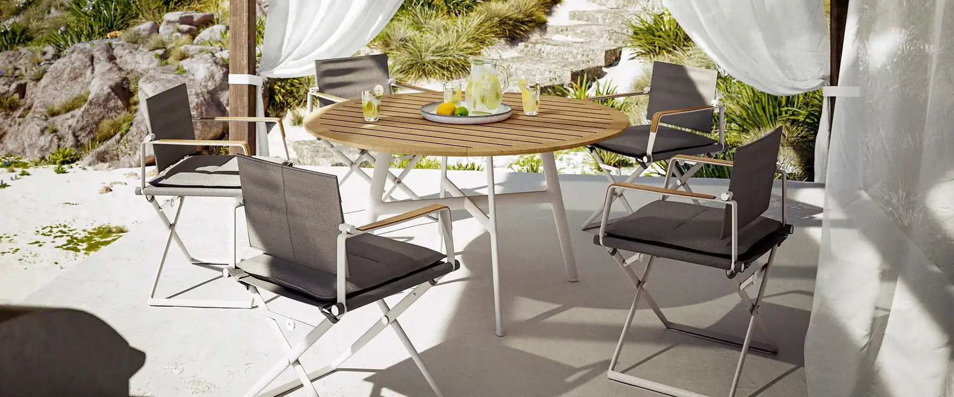 Dedon SEAX folding chairs around a round table on a white terrace with curtains, above a rocky coast