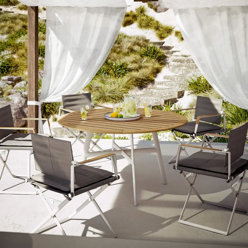 Dedon SEAX folding armchairs around a round teak table under white curtains on a bright terrace