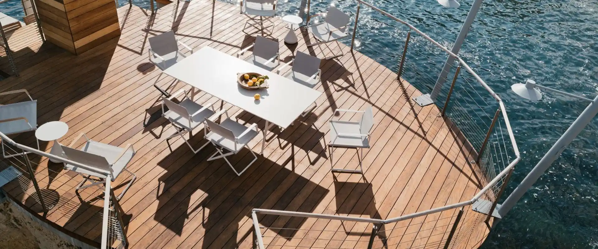 Dedon SEAX folding chairs around a white dining table on a rounded wooden deck above the sea, seen from above