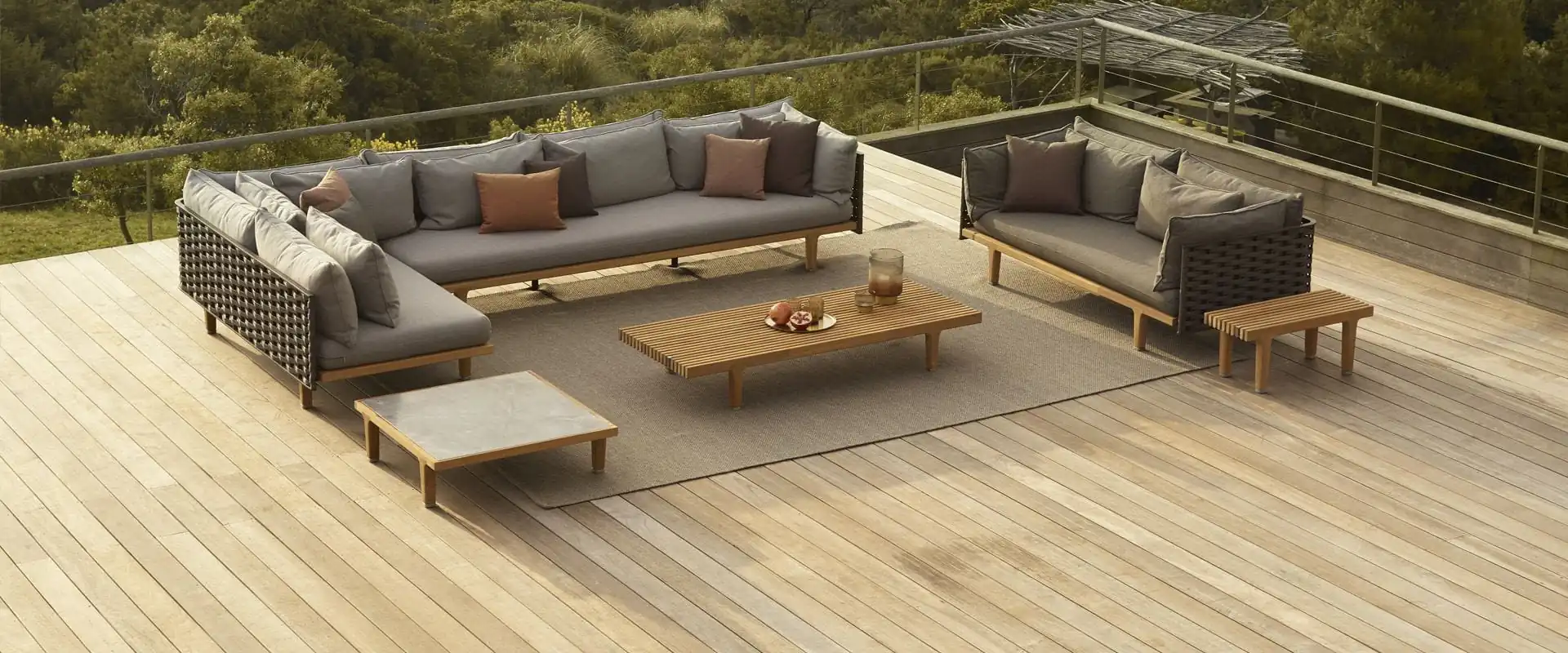 Dedon Sealine modular sofa with a teak coffee table on a wooden deck surrounded by green hills
