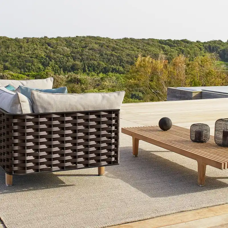 Dedon Sealine sofa in dark woven rope with a slatted teak coffee table on a deck above green hills