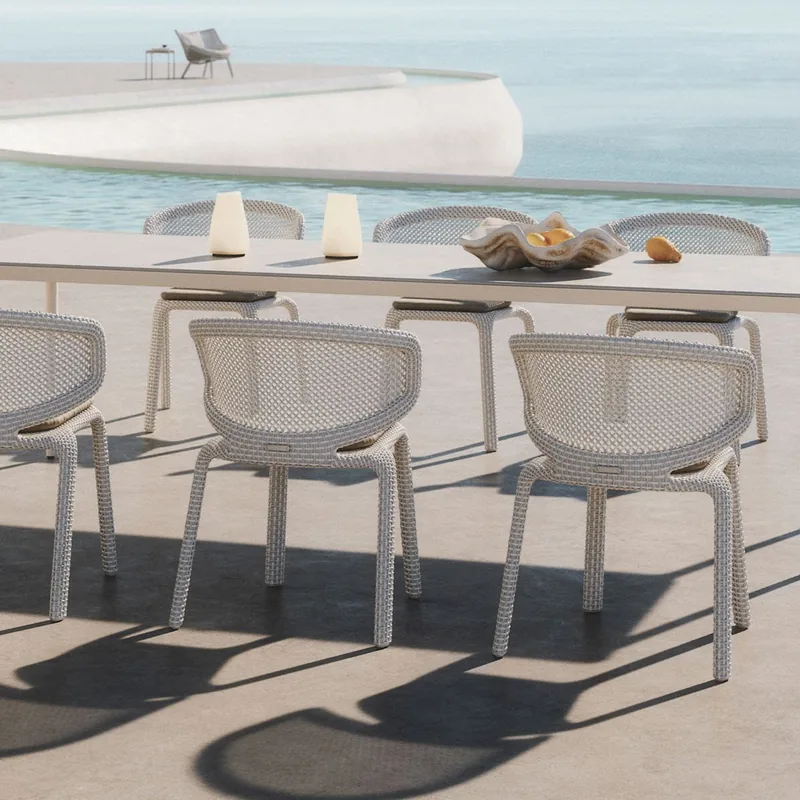 Dedon Seashell dining chairs in white along a table on a pale terrace, with a pool and the sea behind