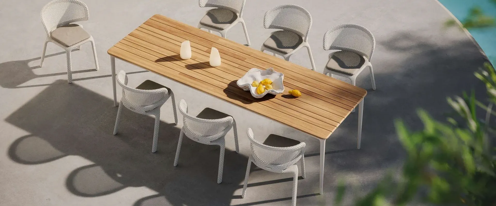 Dedon Seashell dining chairs in white around a long teak table on a sunlit terrace, seen from above