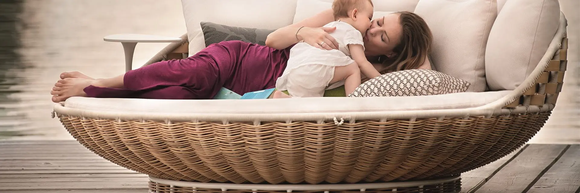 Mother and child lying in a Dedon Swingrest lounger on a wooden dock beside a lake