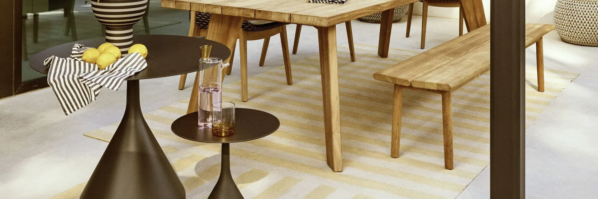 Dedon teak dining table with benches and chairs set for lunch with lemons, on a shaded terrace with potted plants