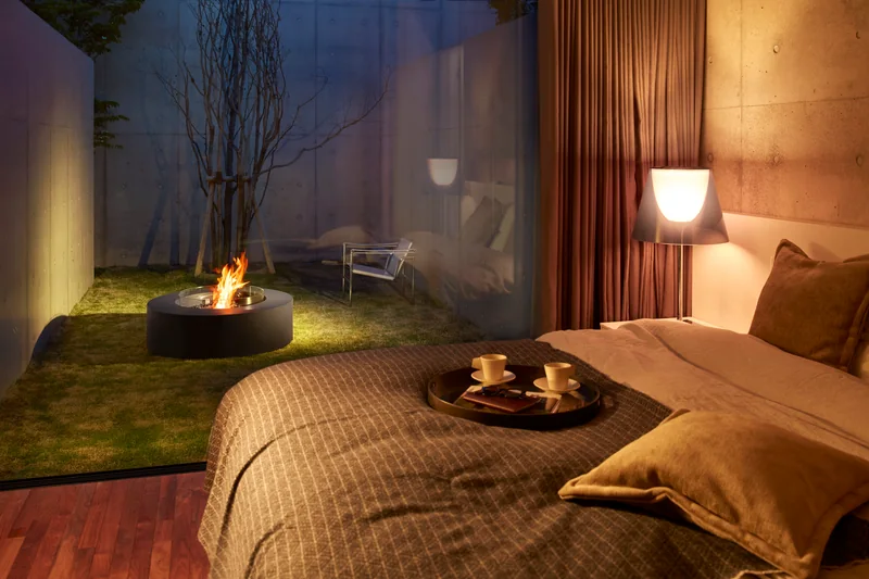 EcoSmart Ark 40 fire table burning on a garden terrace at night, seen from a bedroom with warm lighting