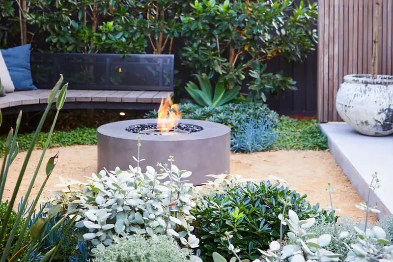 EcoSmart Ark 40 fire table in pale concrete burning in a garden with silver-leaved plants and a curved bench