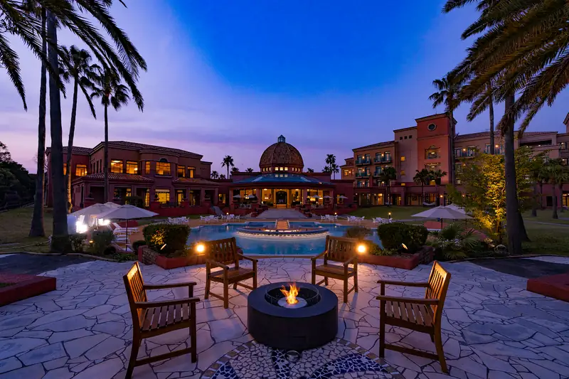 EcoSmart Ark 40 fire table burning between wooden armchairs on a stone terrace at twilight, with a domed hotel behind