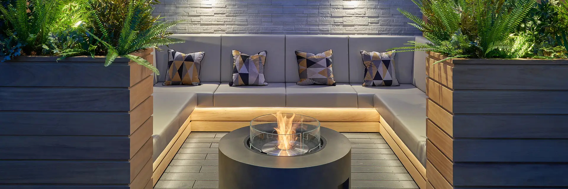 EcoSmart Ark 40 fire table burning in a sunken garden lounge with cushioned benches, planters and wall lights