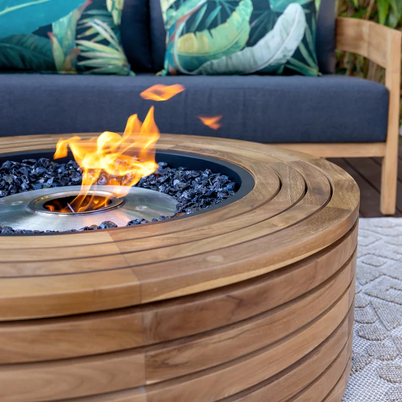 Close view of an EcoSmart Ark 40 fire table in teak with a flame, in front of an outdoor sofa