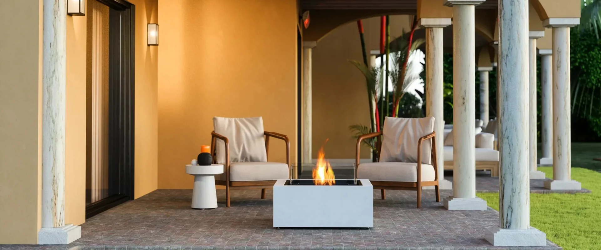 White EcoSmart Base 30 bioethanol fire table burning between two armchairs on the columned porch of an ochre-coloured villa, with a lawn in front