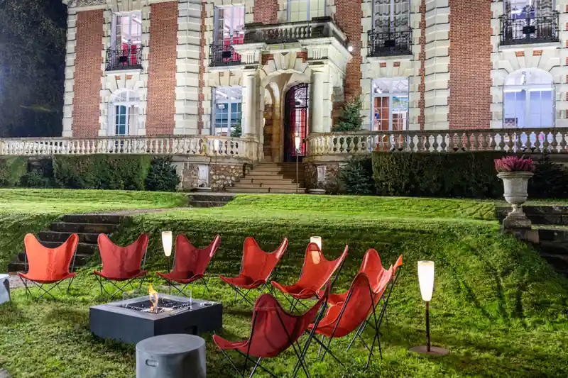 EcoSmart Base 40 fire table on the lawn of a château at dusk, with red butterfly chairs
