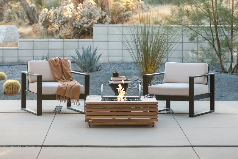 EcoSmart Base 40 fire table in teak between two armchairs on a concrete terrace, with Joshua trees behind