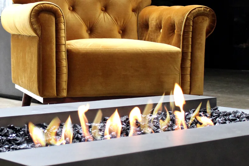 EcoSmart Cosmo 50 fire table with tall flames over black glass, in front of a mustard velvet armchair