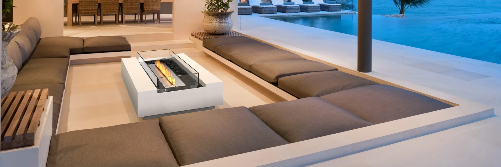 EcoSmart Cosmo 50 fire table in a sunken lounge with brown sofas, open to a pool and the sea at dusk