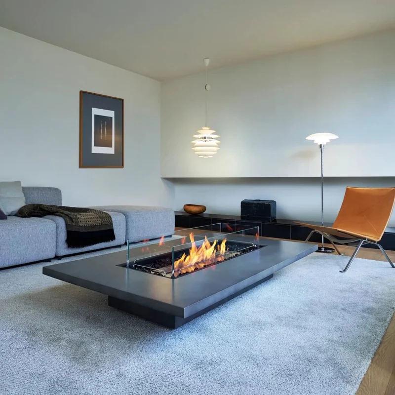 Long EcoSmart Daiquiri 70 fire table in graphite burning on a pale rug in a living room with a leather lounge chair