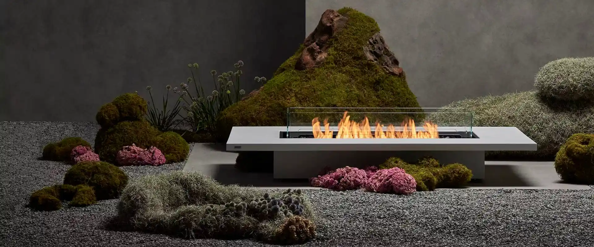 Long EcoSmart Daiquiri 70 fire table with a line of flames in a gravel garden with moss-covered rocks
