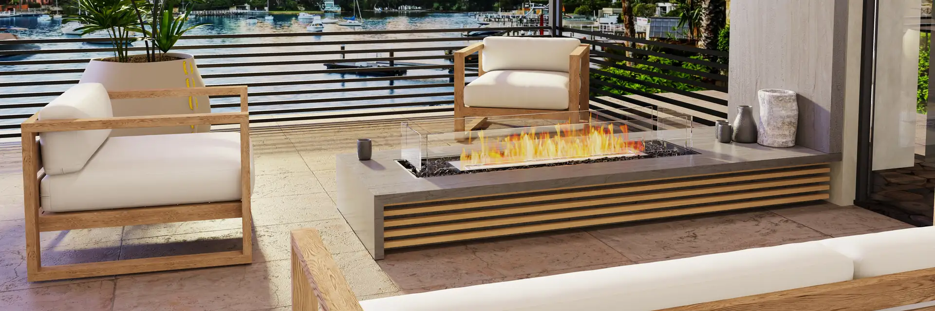 EcoSmart Fire Flex bench fireplace burning on a terrace with teak armchairs and palms, overlooking the water at sunset