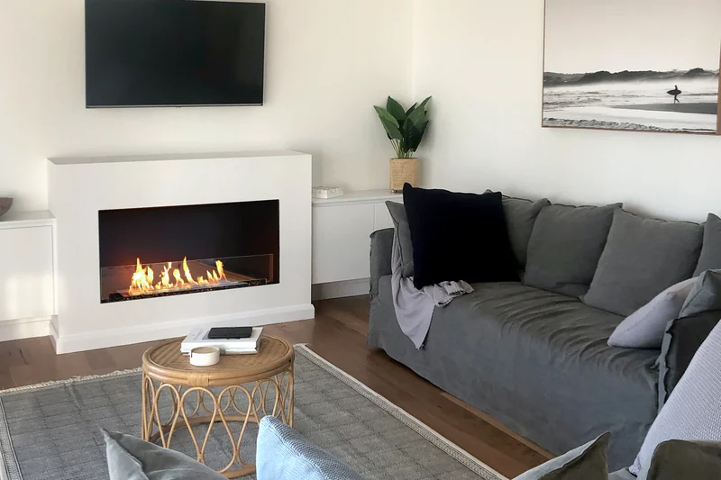 EcoSmart Fire Flex fireplace burning in a white surround below a television, in front of gray sofas