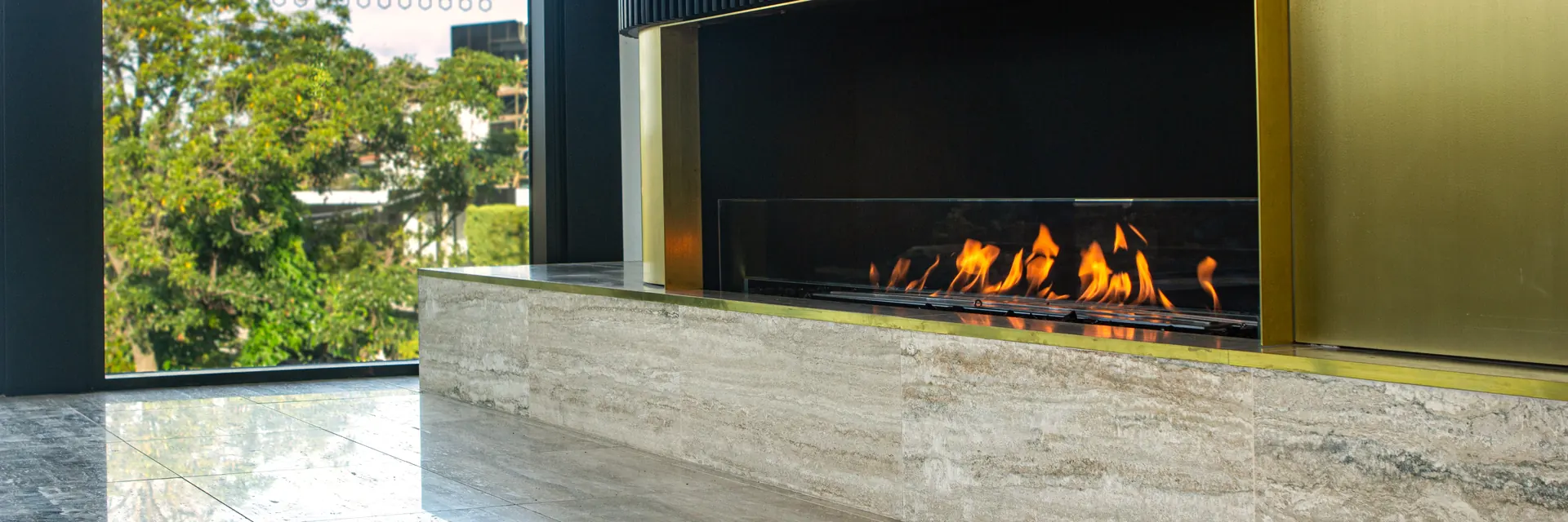 EcoSmart Fire Flex single-sided fireplace burning in a brass surround below a black fluted wall, on a marble hearth