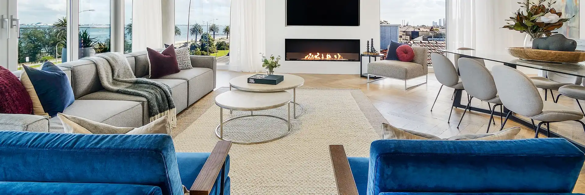 EcoSmart Fire Flex single-sided fireplace burning in the white wall of a bright living room with blue velvet armchairs and wide windows
