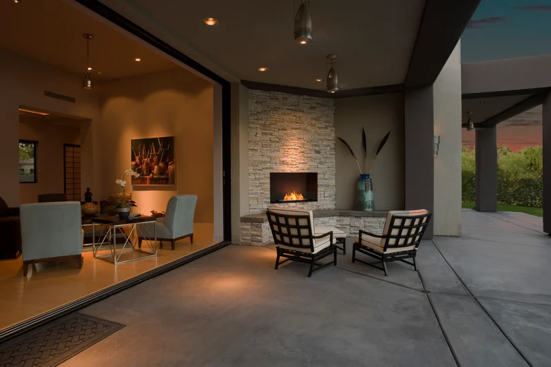 EcoSmart Fire Flex fireplace burning in a stone wall on a covered terrace with armchairs at dusk