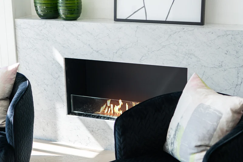 EcoSmart Fire Flex fireplace burning in a pale marble surround, with two dark velvet armchairs in front