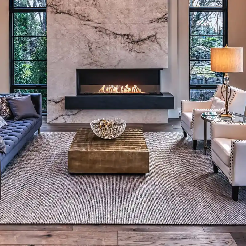 EcoSmart Fire Flex bioethanol fireplace set into a veined marble surround in a tall living room with black-framed windows, facing a pair of white armchairs